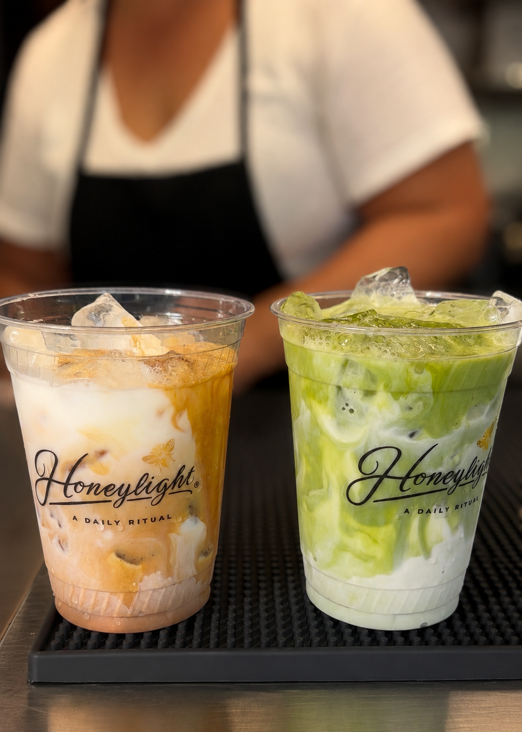 Two Honeylight branded cups with a barista crafting drinks in the background